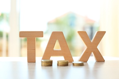 Photo of Word TAX and coins on table against blurred background