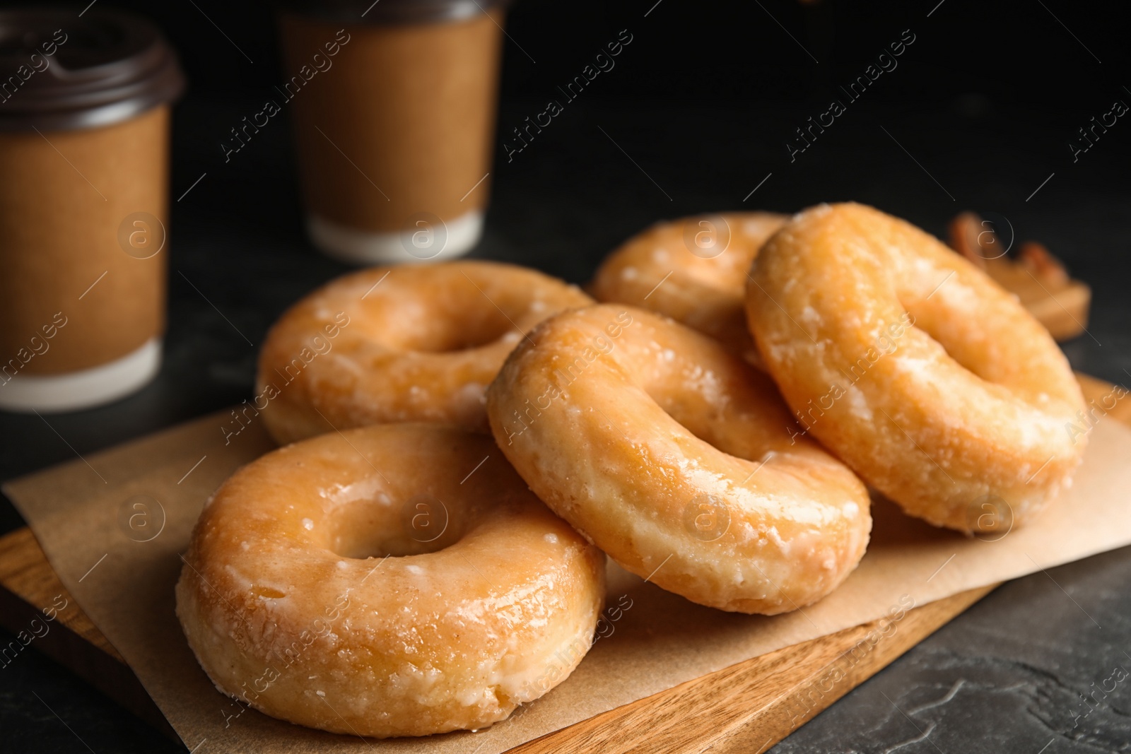 Photo of Delicious glazed donuts on wooden board, closeup