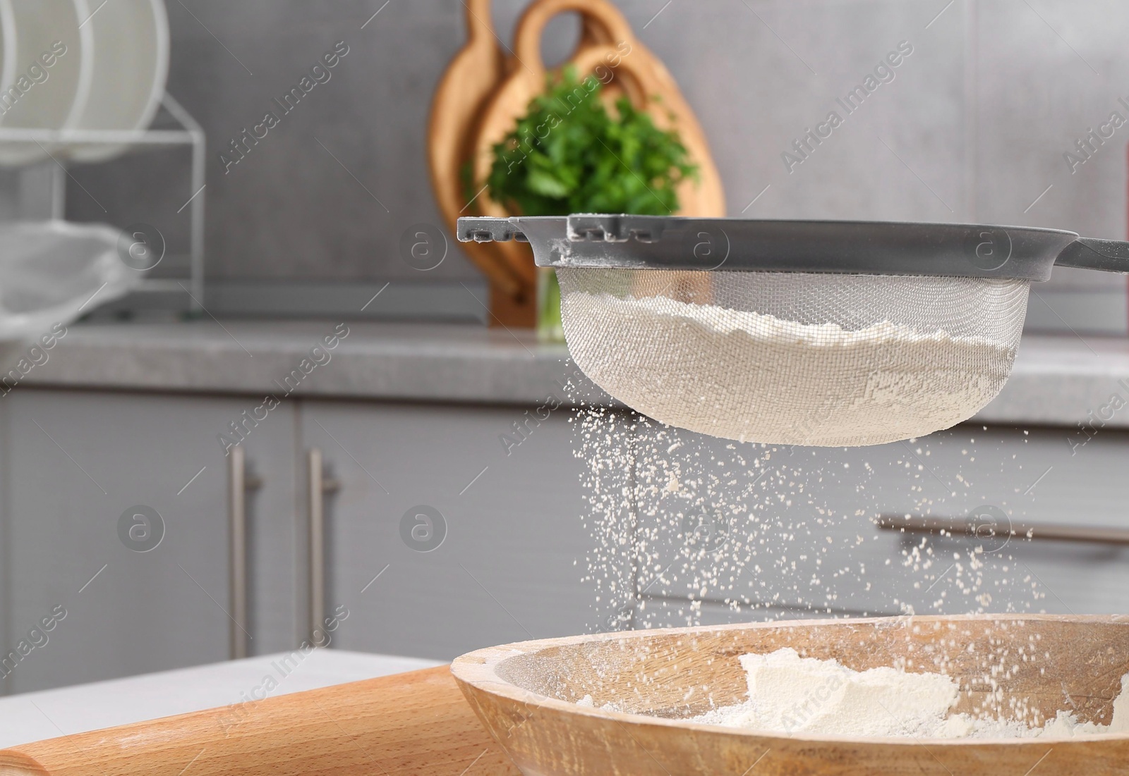 Photo of Woman sieving flour into bowl at white wooden table in kitchen, closeup