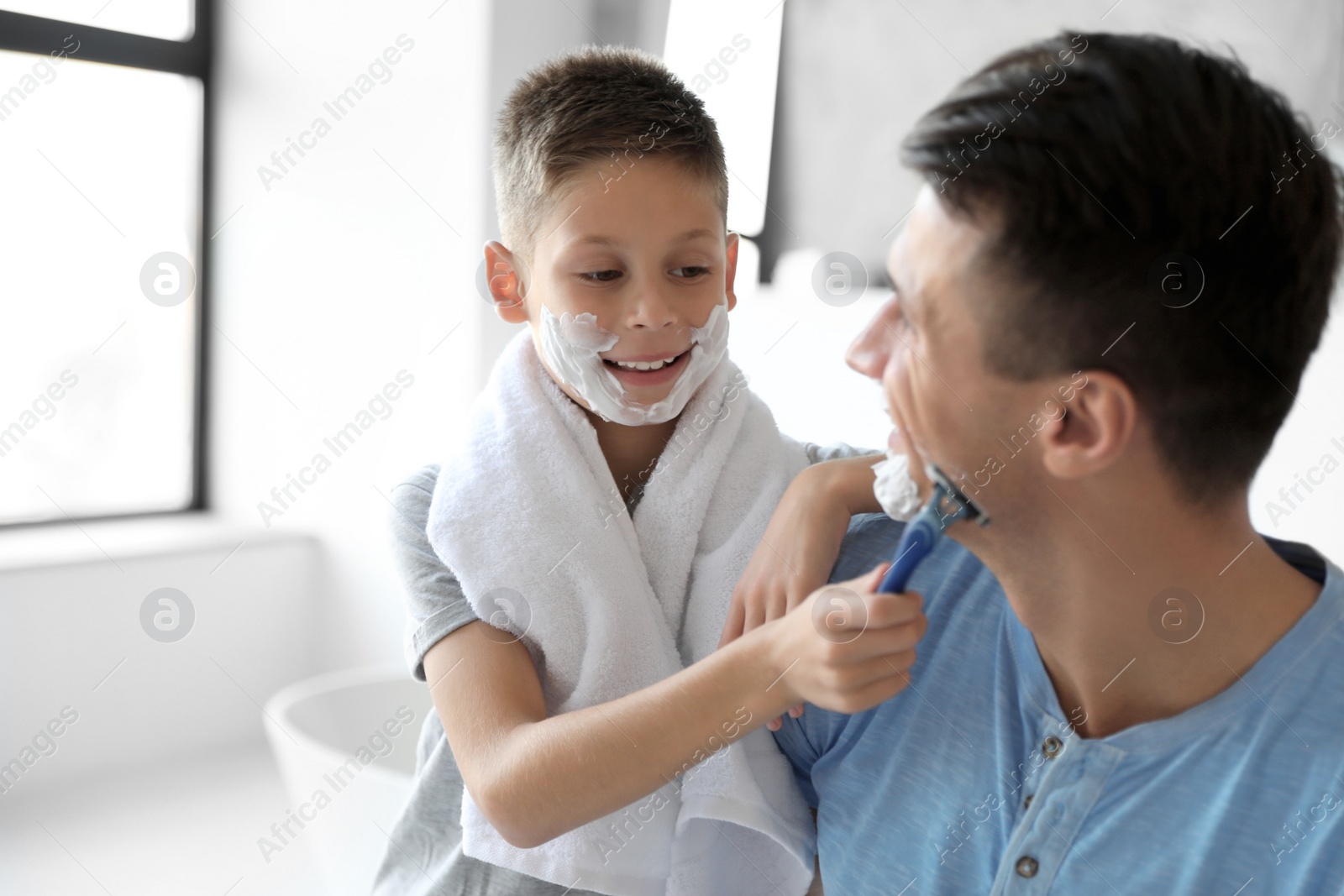 Photo of Son shaving his father with razor in bathroom