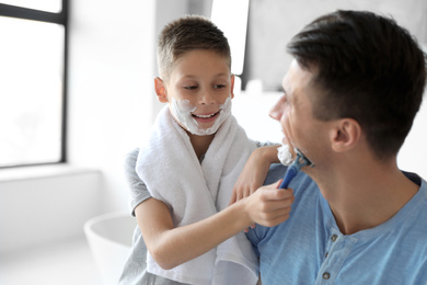 Photo of Son shaving his father with razor in bathroom