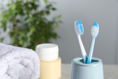 Photo of Plastic toothbrushes in holder, towel and cosmetic product on table, closeup