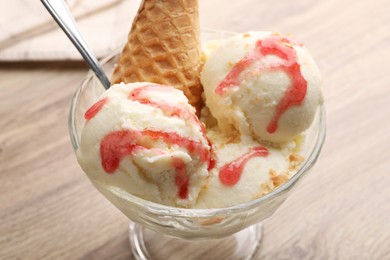 Photo of Delicious scoops of vanilla ice cream with wafer cone and strawberry topping in glass dessert bowl on wooden table, closeup