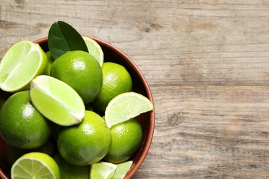 Tasty ripe limes in bowl on wooden table, top view. Space for text
