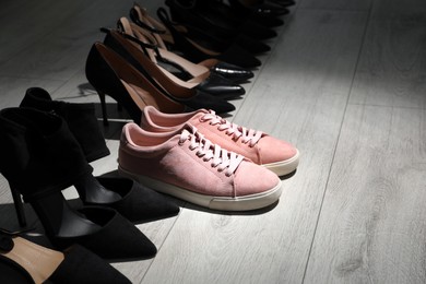 Photo of Sportive sneakers among high heeled shoes on light wooden floor. Diversity concept