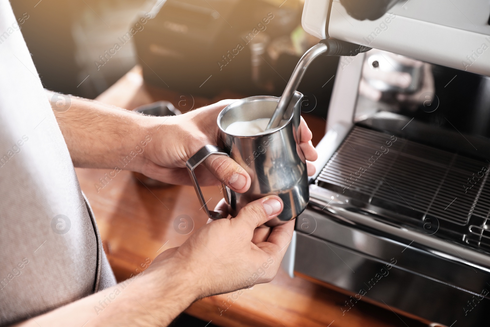 Photo of Barista frothing milk in metal pitcher with coffee machine wand at bar counter, closeup