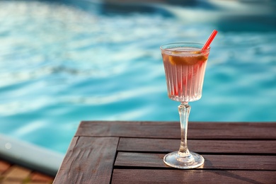 Glass of fresh summer cocktail on wooden table near swimming pool outdoors. Space for text