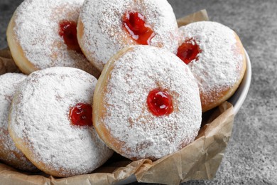 Photo of Delicious donuts with jelly and powdered sugar in bowl on grey table, closeup