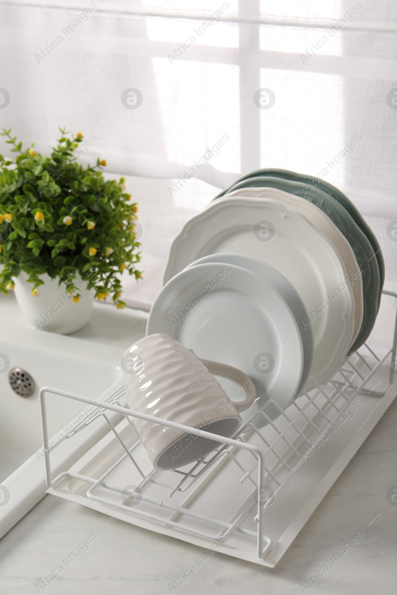 Photo of Drainer with different clean dishware, cup and houseplant on light table indoors