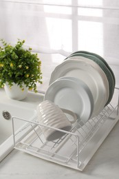 Photo of Drainer with different clean dishware, cup and houseplant on light table indoors