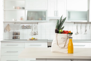 Photo of Textile shopping bag full of vegetables and juice on table in kitchen. Space for text