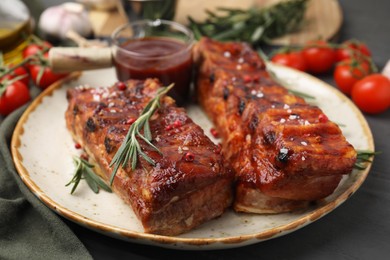 Photo of Tasty roasted pork ribs served with sauce and rosemary on grey wooden table, closeup