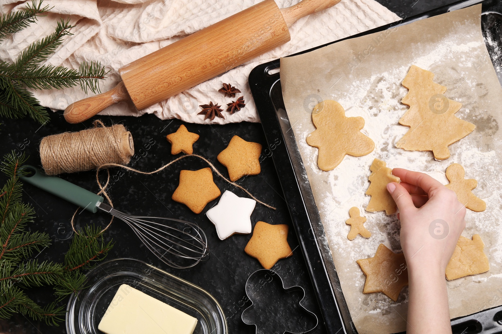 Photo of Woman putting raw Christmas cookies on baking tray at dark table, top view