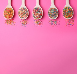 Photo of Colorful sprinkles in spoons on pink background, flat lay with space for text. Confectionery decor