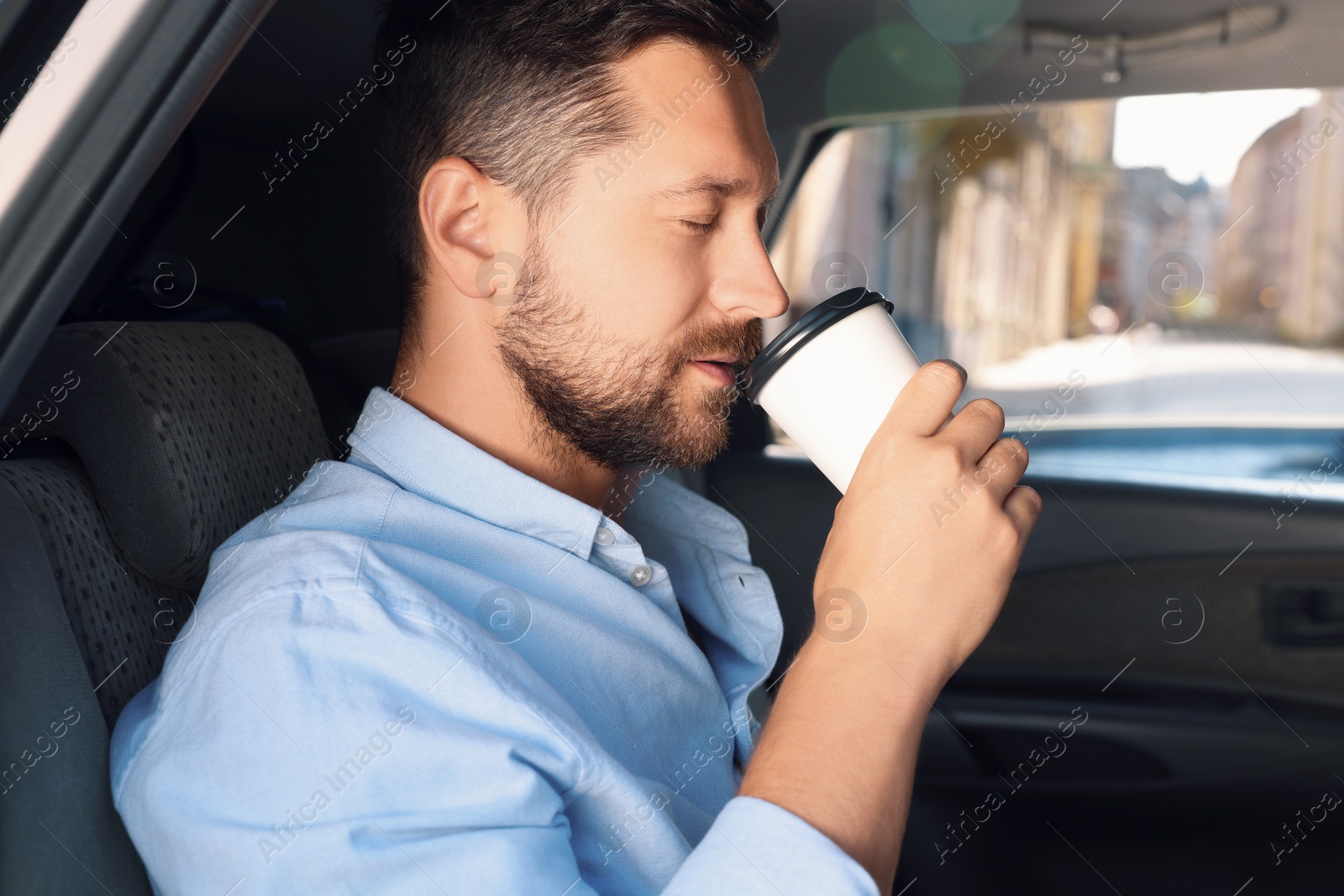 Photo of To-go drink. Handsome man drinking coffee in car