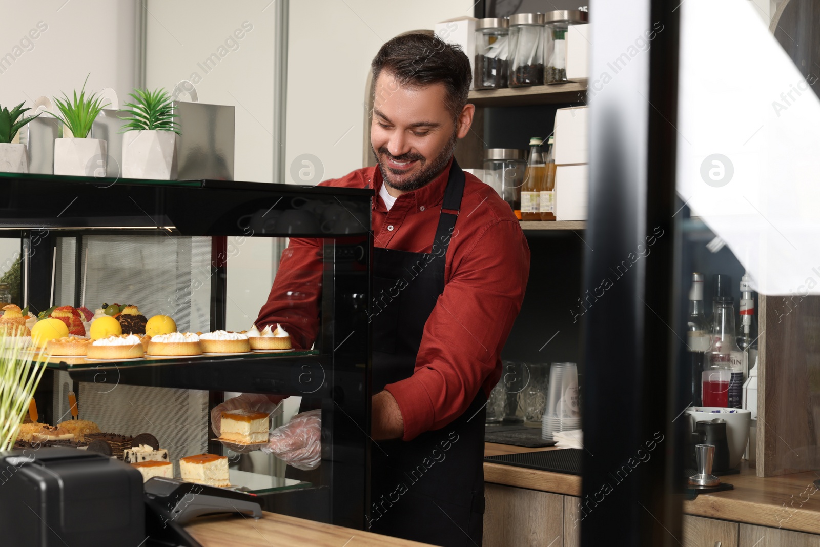 Photo of Business owner in his cafe. Happy man taking tasty piece of cheesecake from showcase