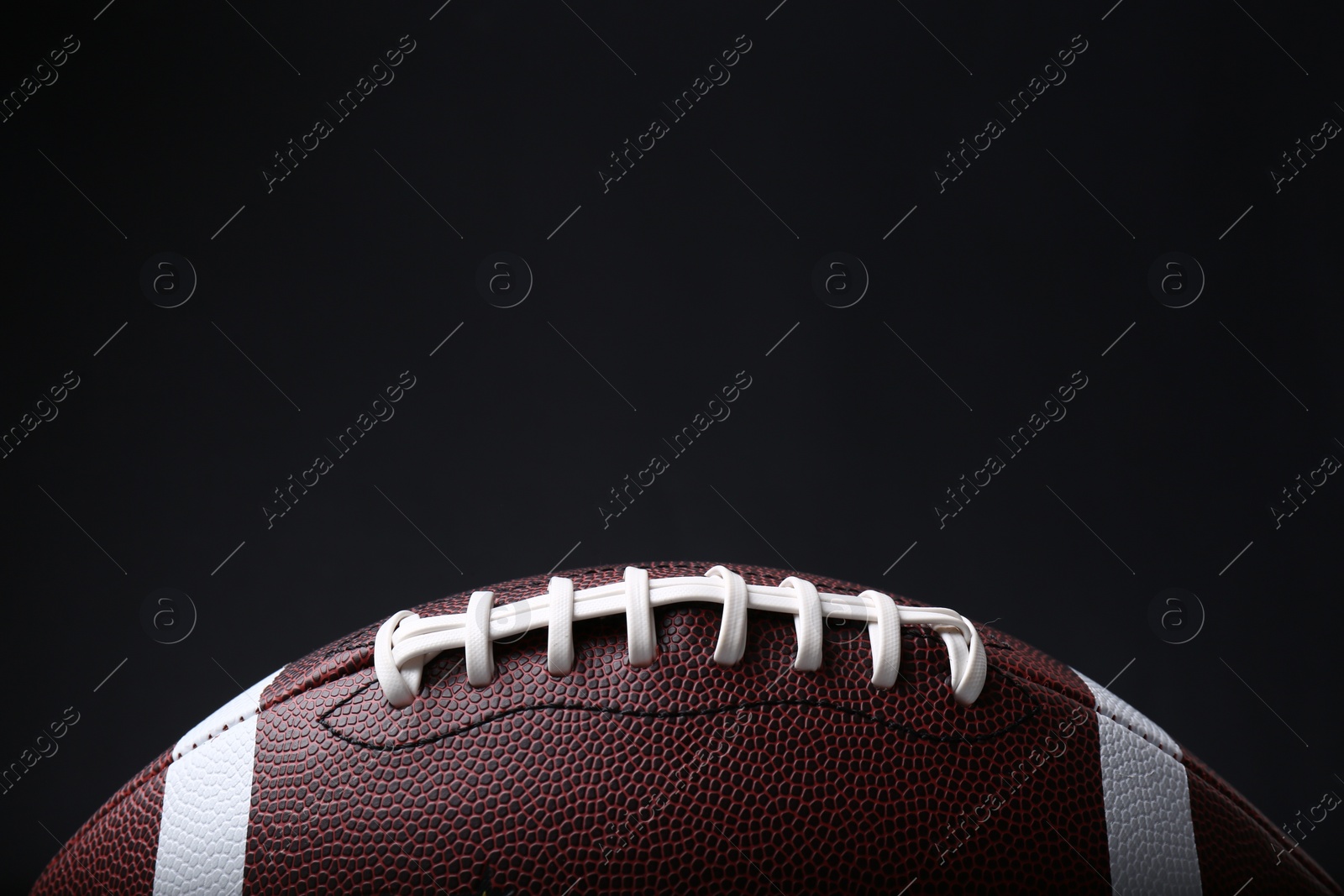 Photo of American football ball on black background, closeup. Space for text