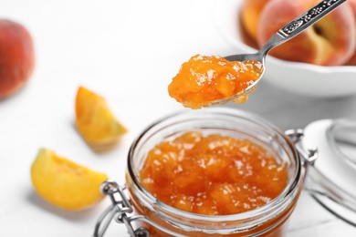 Photo of Jar and spoon with tasty peach jam on table