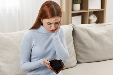 Upset woman with empty wallet on sofa indoors