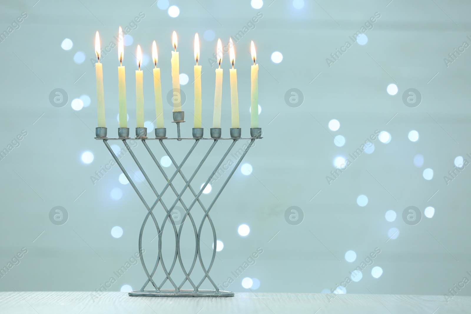 Photo of Hanukkah celebration. Menorah with burning candles on table against blurred lights, space for text