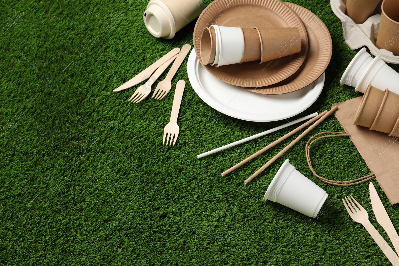 Photo of Eco disposable tableware on green artificial grass. Space for text