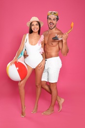 Photo of Young attractive couple in beachwear with snorkel and ball on pink background
