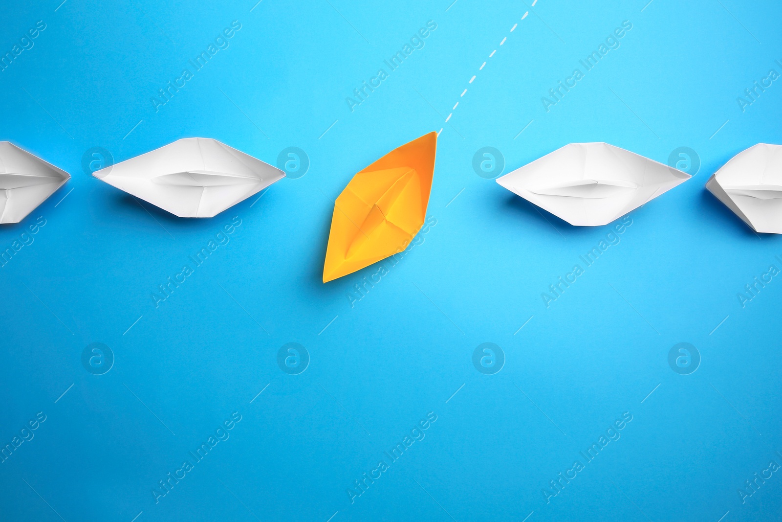 Photo of Yellow paper boat floating through others on light blue background, flat lay with space for text. Uniqueness concept