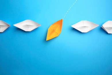 Photo of Yellow paper boat floating through others on light blue background, flat lay with space for text. Uniqueness concept