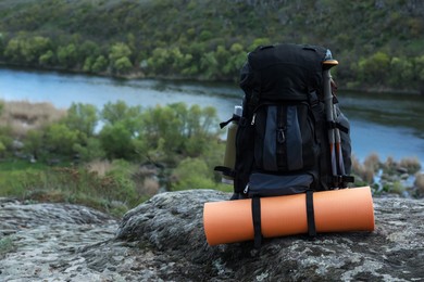Photo of Backpack with camping mat and trekking poles on rocky hill, space for text