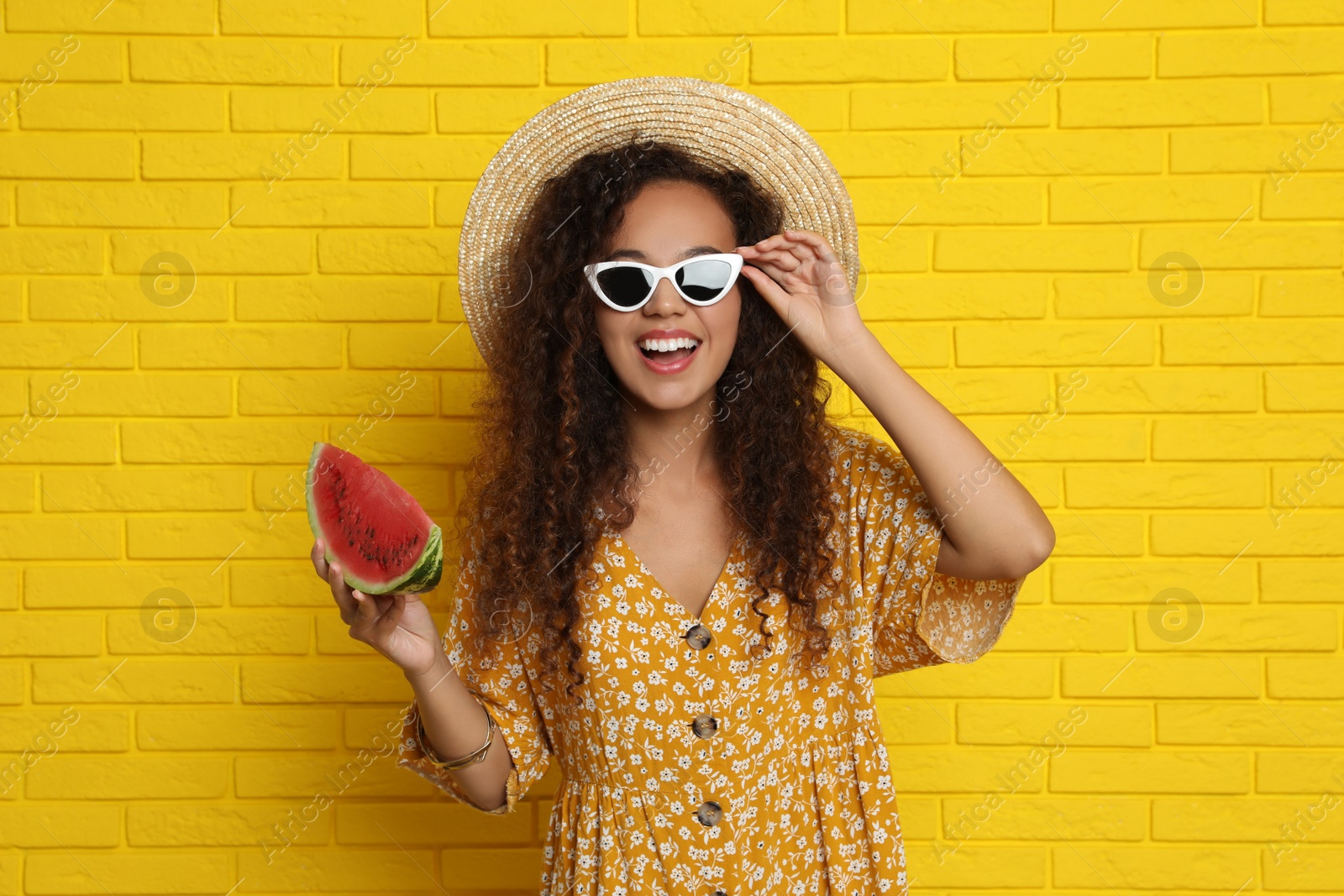 Photo of Beautiful young African-American woman with watermelon near yellow brick wall