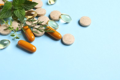 Different pills and herbs on light blue background, space for text. Dietary supplements