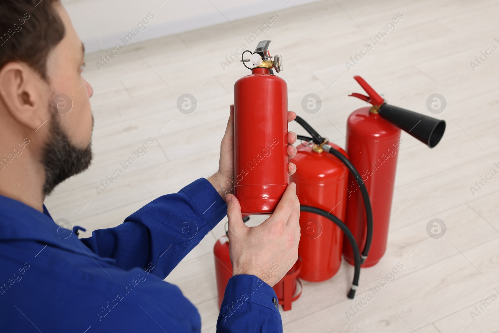 Photo of Man checking quality of fire extinguishers indoors, closeup