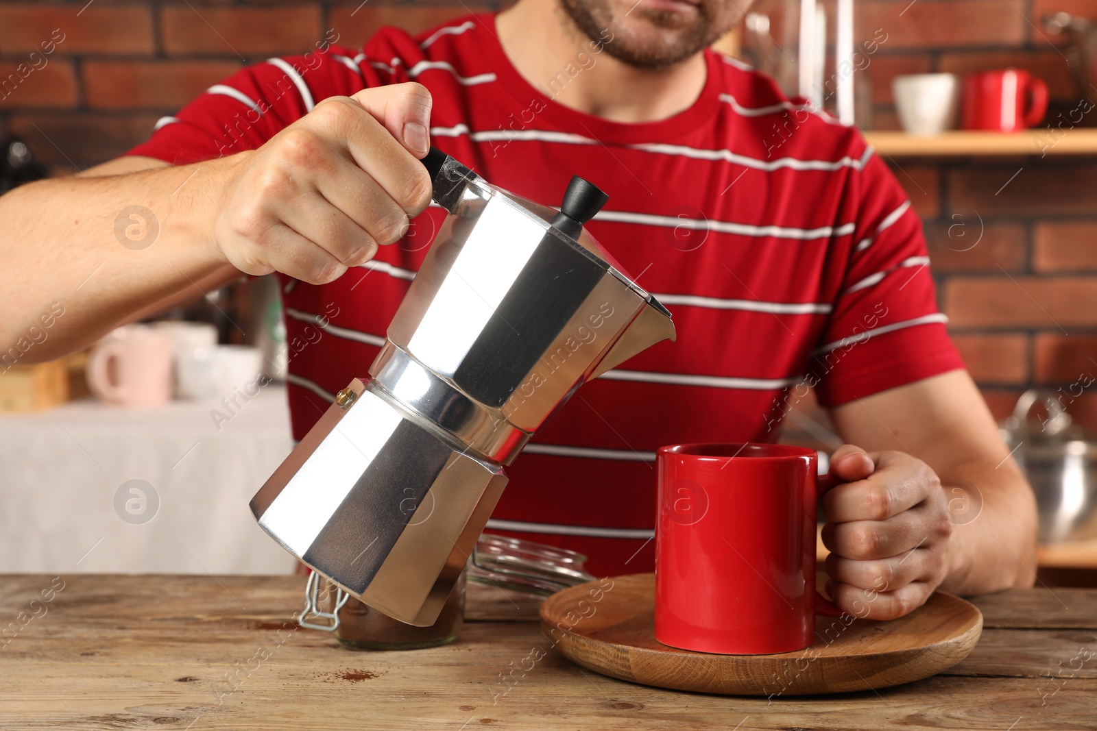 Photo of Man pouring aromatic coffee from moka pot into cup at wooden table indoors, closeup