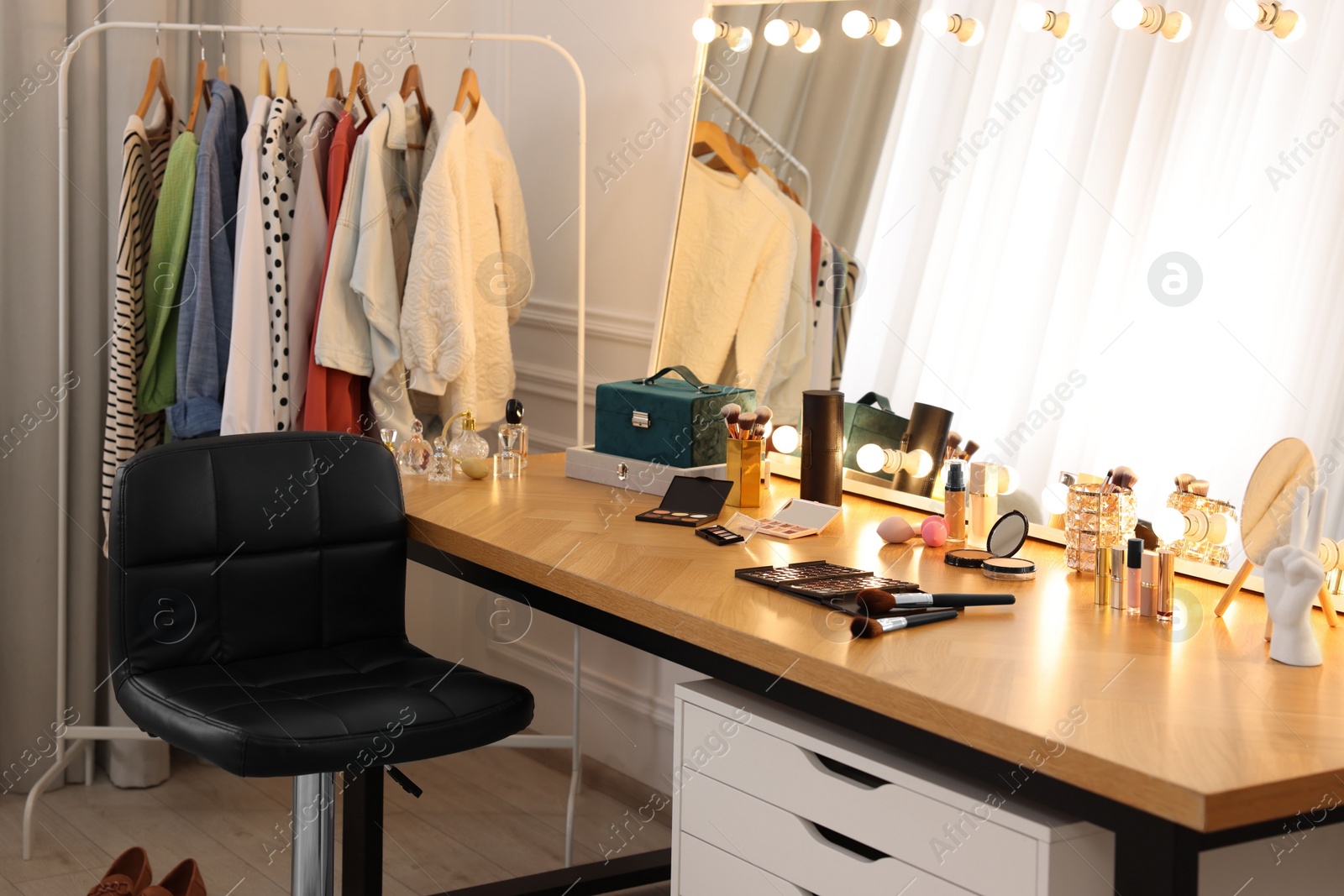 Photo of Makeup room. Stylish dressing table with mirror, chair and clothes rack