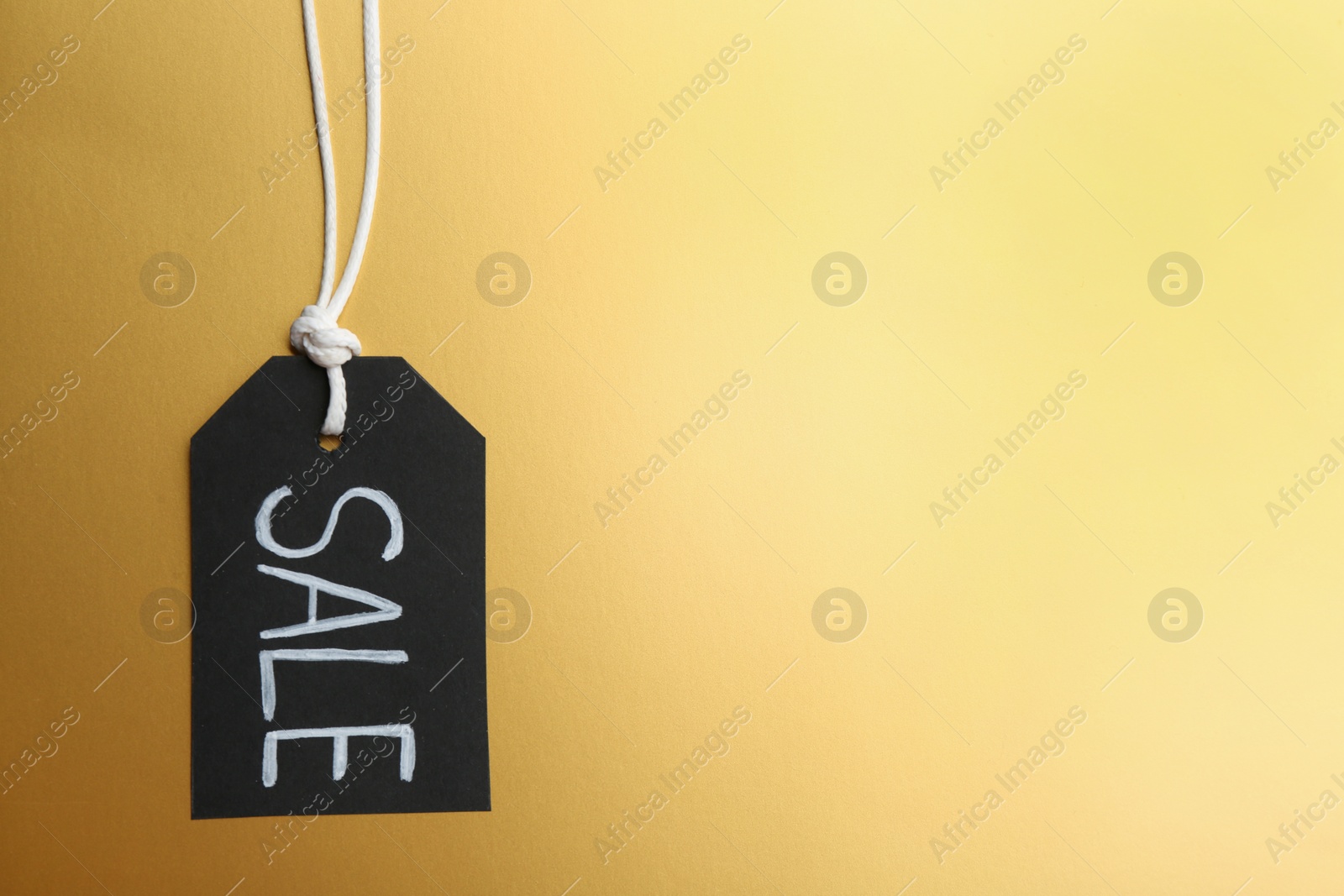 Photo of Top view of tag with word SALE on golden background, space for text. Black Friday concept