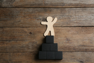 Human figure and pyramid on wooden background, flat lay. Career promotion concept