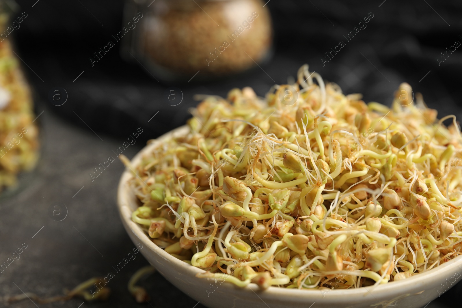 Photo of Bowl of sprouted green buckwheat on grey table, closeup