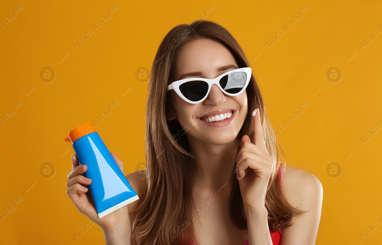 Photo of Young woman applying sun protection cream on orange background