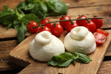 Photo of Delicious burrata cheese with basil and cherry tomatoes on wooden table, closeup