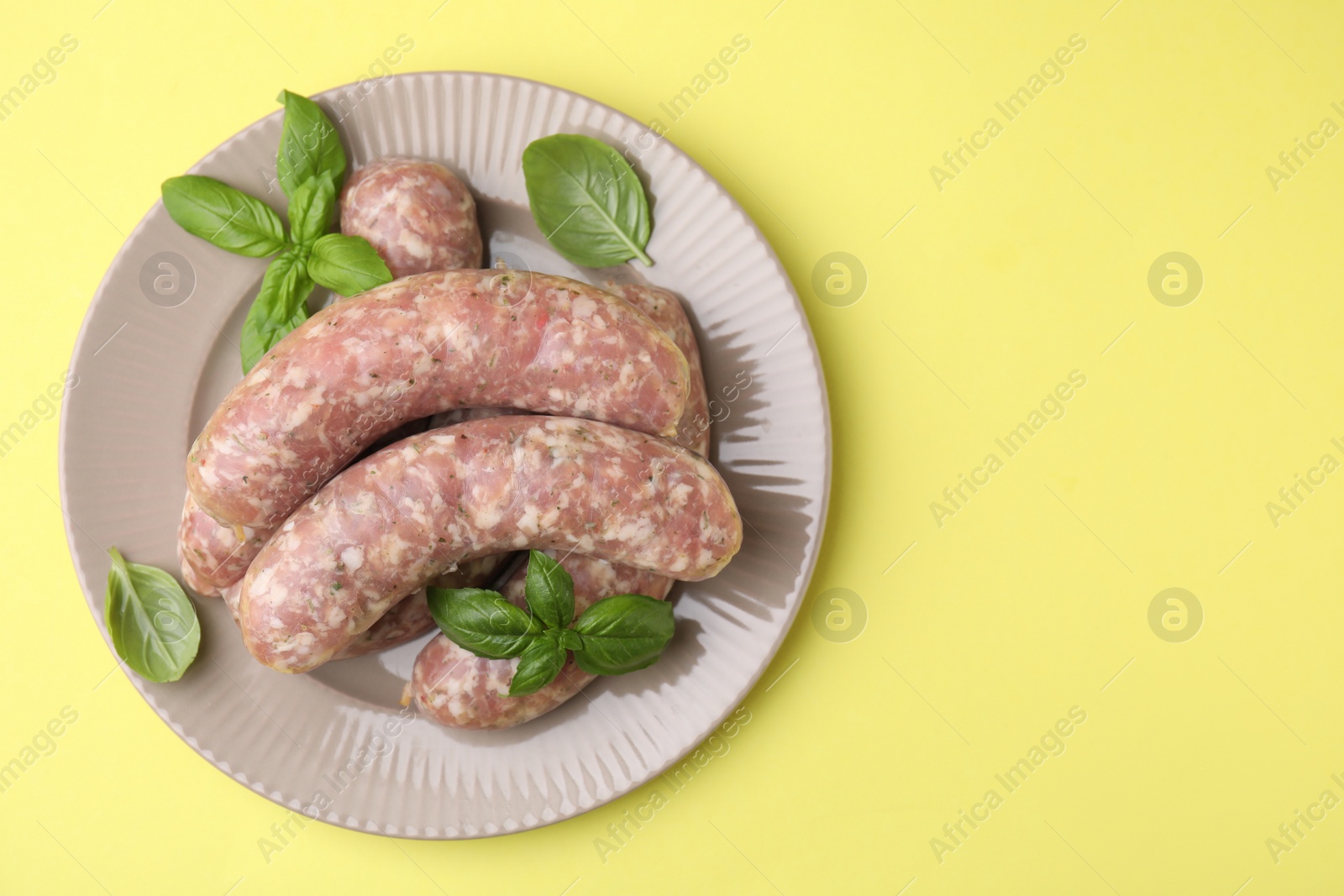 Photo of Raw homemade sausages and basil leaves on yellow background, top view. Space for text