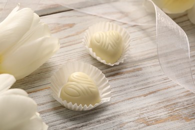 Delicious heart shaped chocolate candies and beautiful tulips on white wooden table, closeup