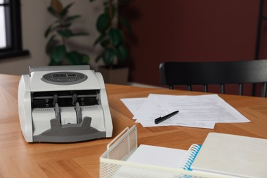 Photo of Modern banknote counter on wooden table indoors