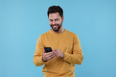 Photo of Happy young man using smartphone on light blue background