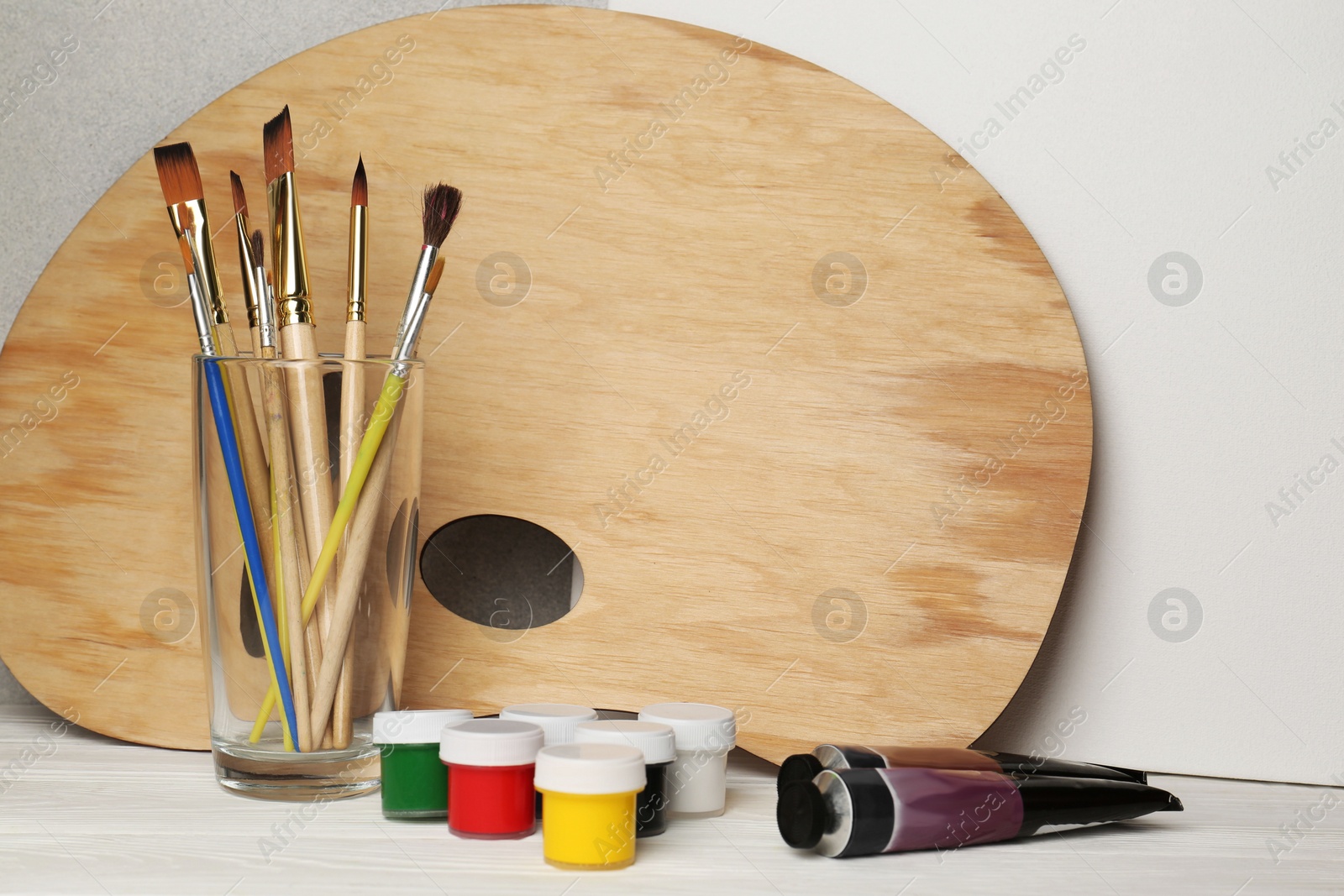 Photo of Artist's palette, colorful paints and brushes on white wooden table