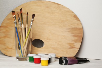 Photo of Artist's palette, colorful paints and brushes on white wooden table