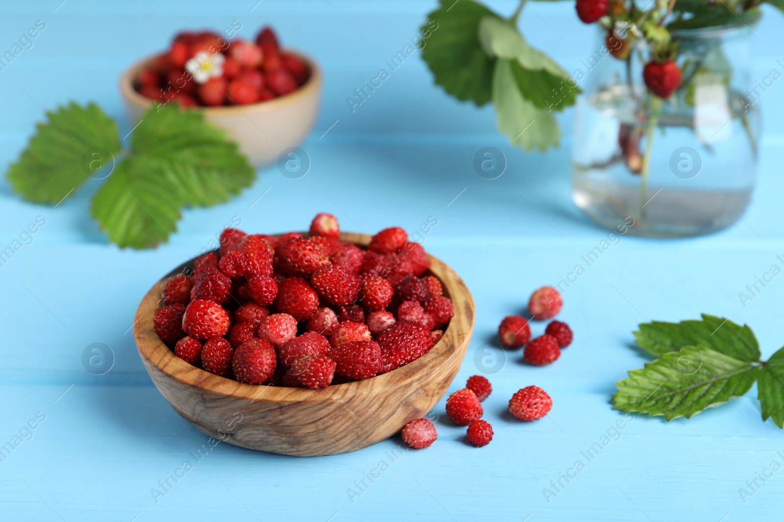 Photo of Fresh wild strawberries in bowl on light blue table