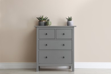 Photo of Grey chest of drawers with houseplants near beige wall