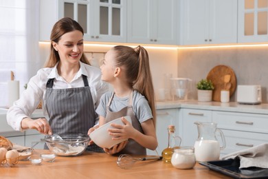 Photo of Making bread. Mother and her daughter preparing dough at wooden table in kitchen