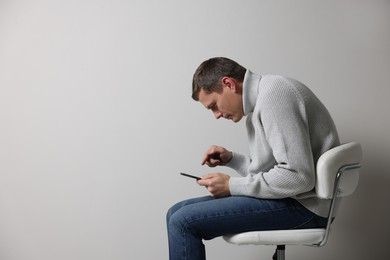 Photo of Man with bad posture using tablet while sitting on chair against grey background. Space for text