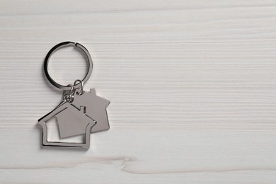 Photo of Metal keychain in shape of houses on white wooden table, top view. Space for text